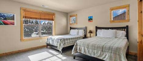 A bedroom with two beds, a window with blinds, a ceiling light, and a small picture on the wall.