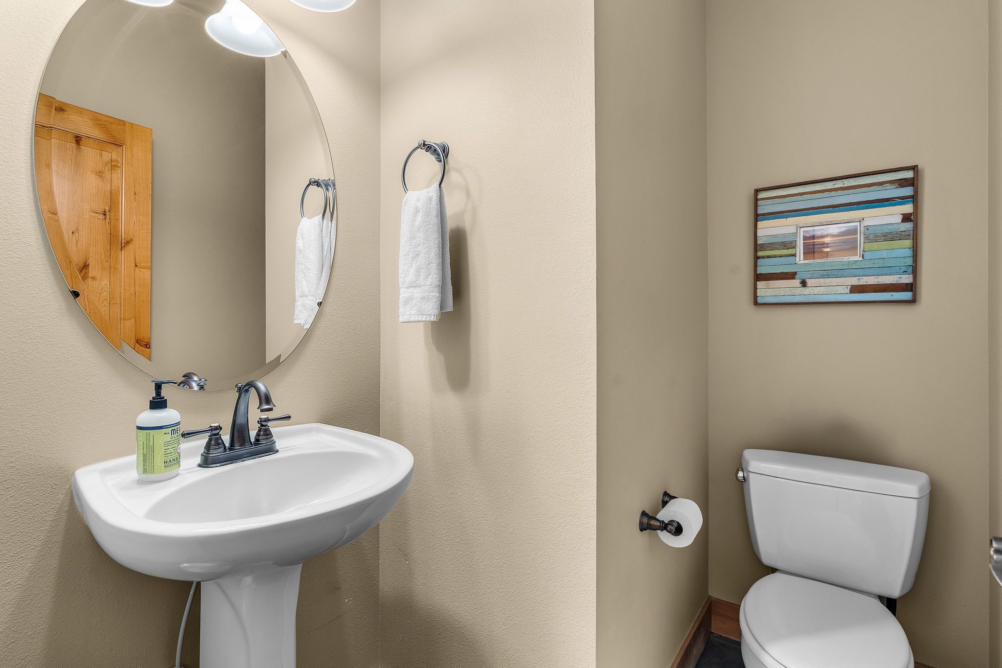 Une salle de bain avec un lavabo blanc, une porte en bois, un miroir, un porte-serviettes et des toilettes.