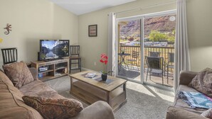 Un salon équipé d’un téléviseur, d’un canapé, d’une table basse et d’un balcon aménagé avec du mobilier d’extérieur.
