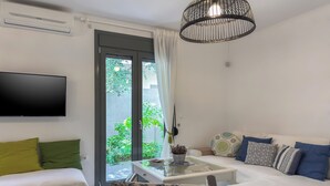 A modern living room with a flat-screen TV, a glass coffee table, a sofa with patterned cushions, and a view of greenery outside. - Alisahni Villa (Daratsos)