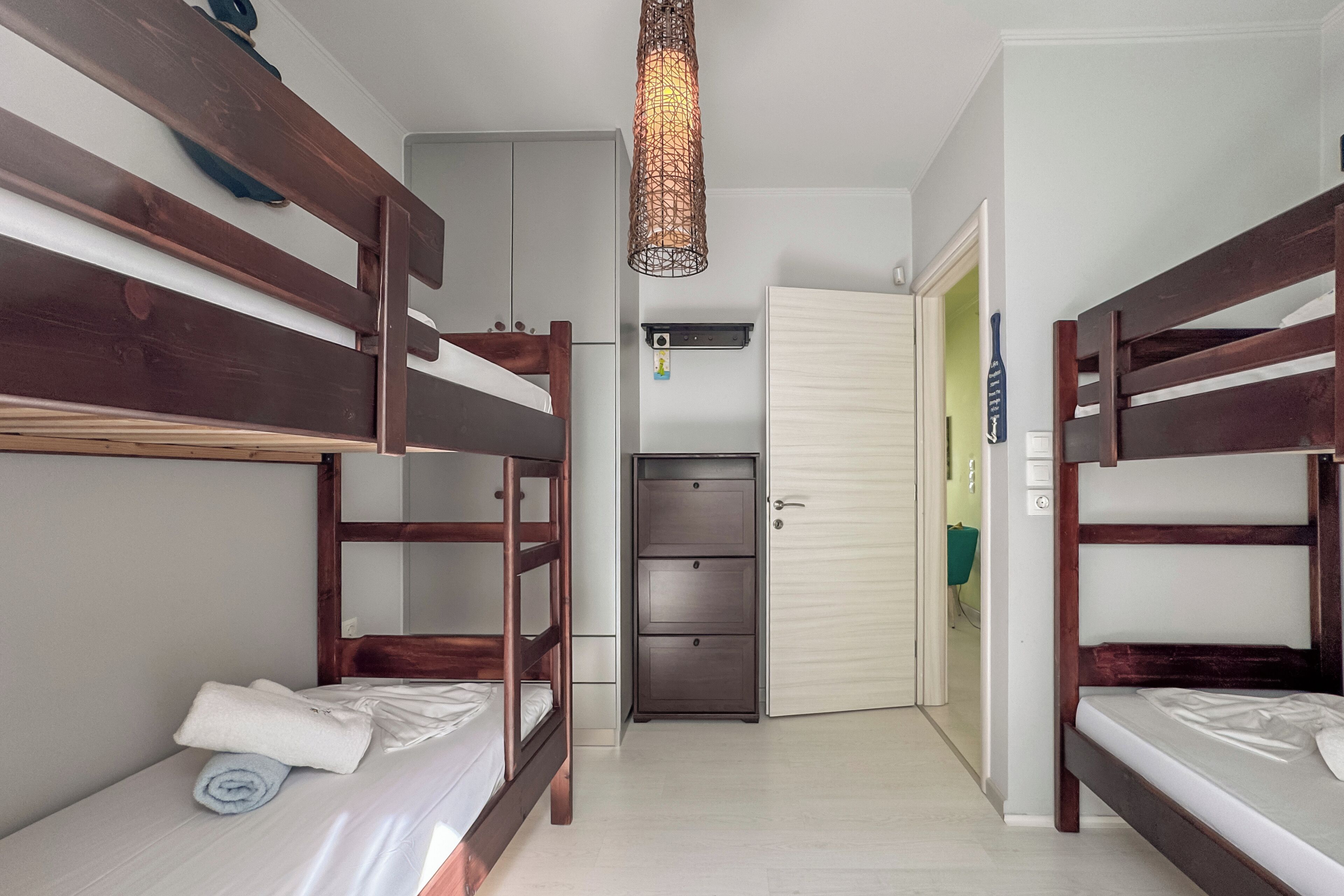 Une chambre avec des lits superposés, un petit bureau et une porte donnant sur une autre pièce.