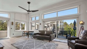 Ein geräumiges Wohnzimmer mit großem Fenster, Deckenventilator und Blick ins Freie.