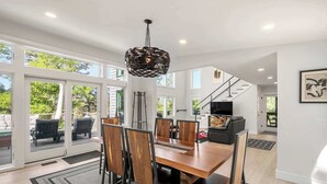 Un comedor amplio con una mesa y sillas de madera, una lámpara moderna y vistas al exterior a través de amplios puertas corredizas de vidrio.