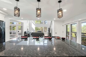 A spacious living area with a large central island, black leather sofas, and a dining table set with red and black plates.