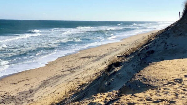 A beach with waves crashing onto the shore, a sandy path leading to the water, and a clear sky.