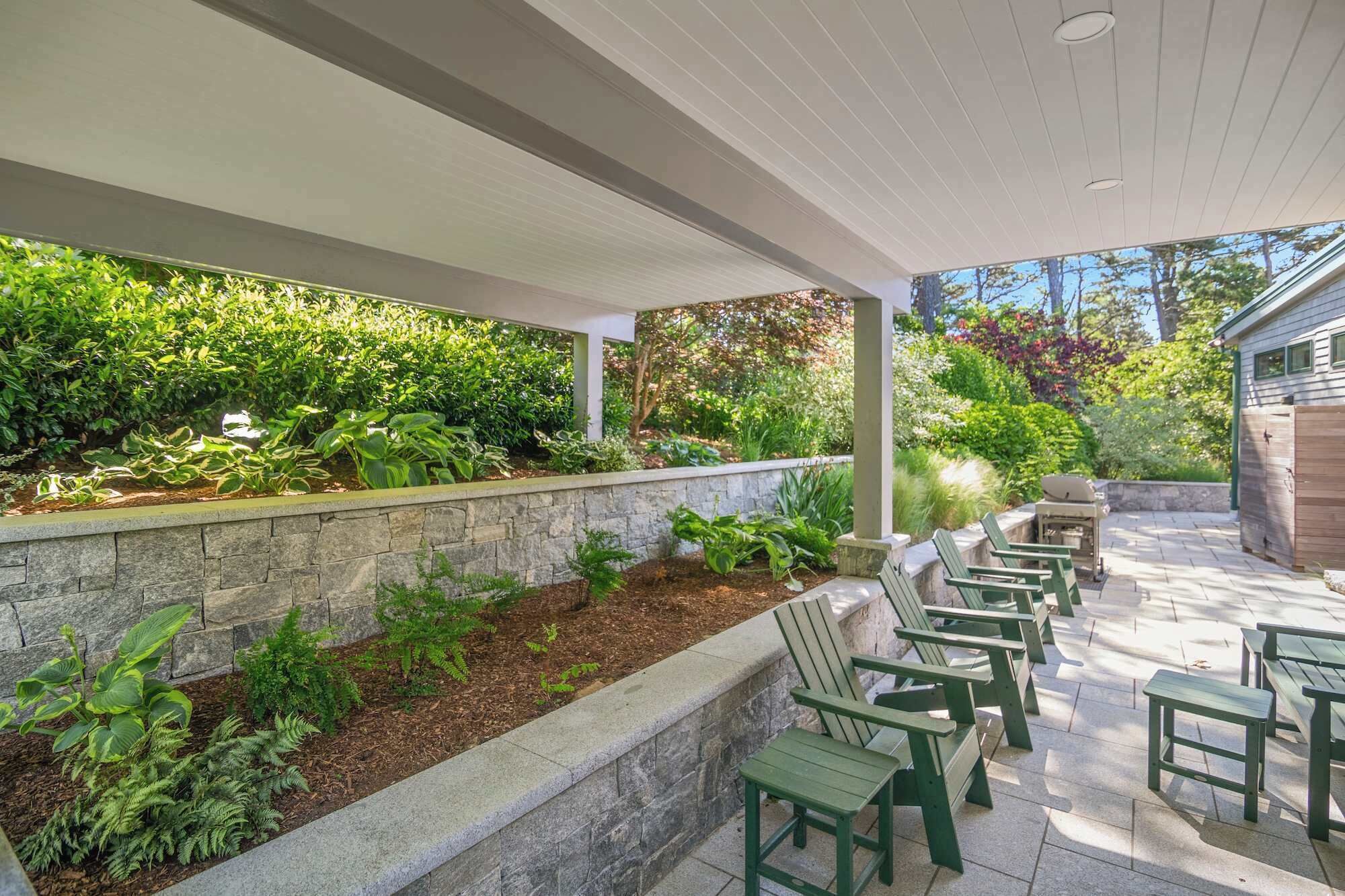 An outdoor patio with stone walls, green chairs, and a barbecue grill.