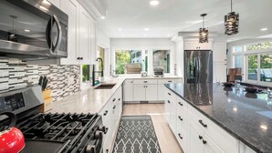 Una cocina moderna con armarios blancos, estufa de acero inoxidable, cocina a gas y una isla grande con encimera negra.