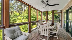 Una terraza techada al aire libre con una mesa de comedor y sillas, ventanas amplias y un ventilador de techo.