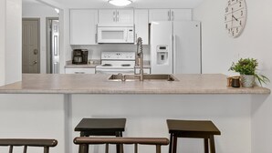 Una cocina moderna con armarios blancos, una isla central, cafetera, refrigerador y un reloj en la pared.