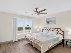Un dormitorio con cama, ventilador de techo, ventana con vistas y un cuadro en la pared.