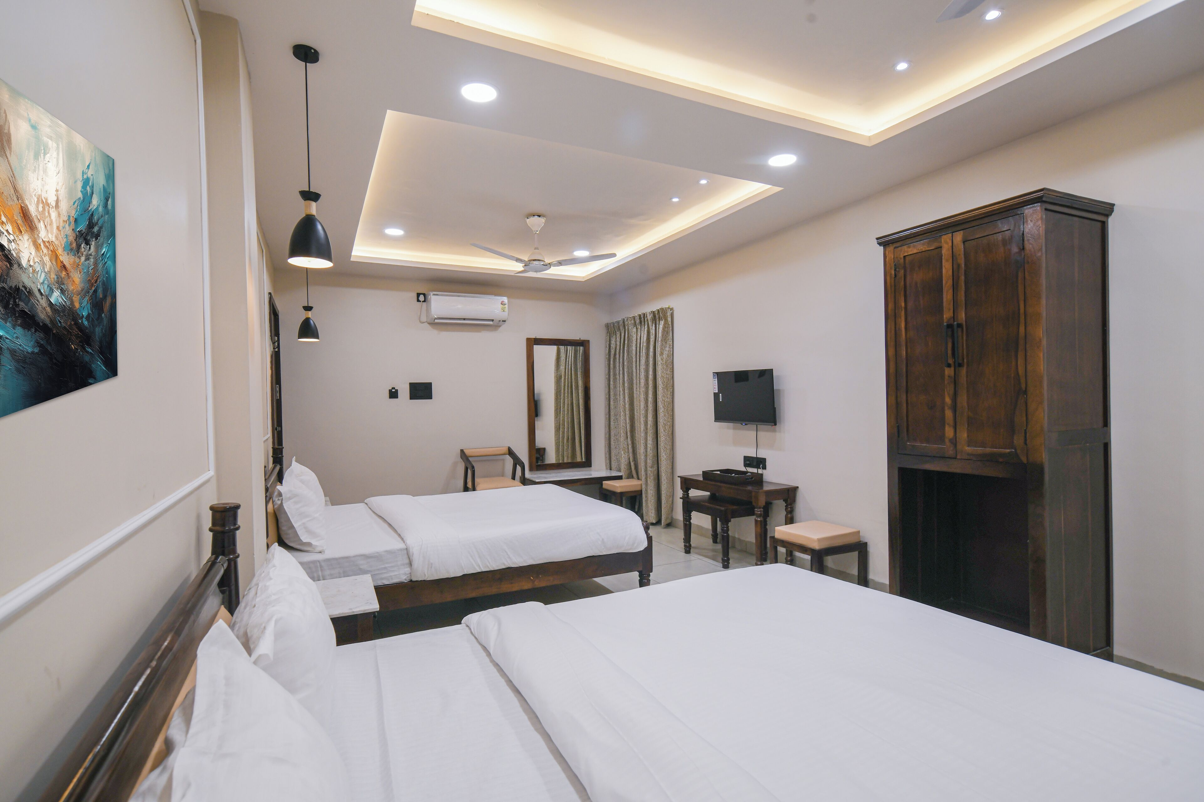 A hotel room with two beds, a desk, a wardrobe, a ceiling fan, and a TV.