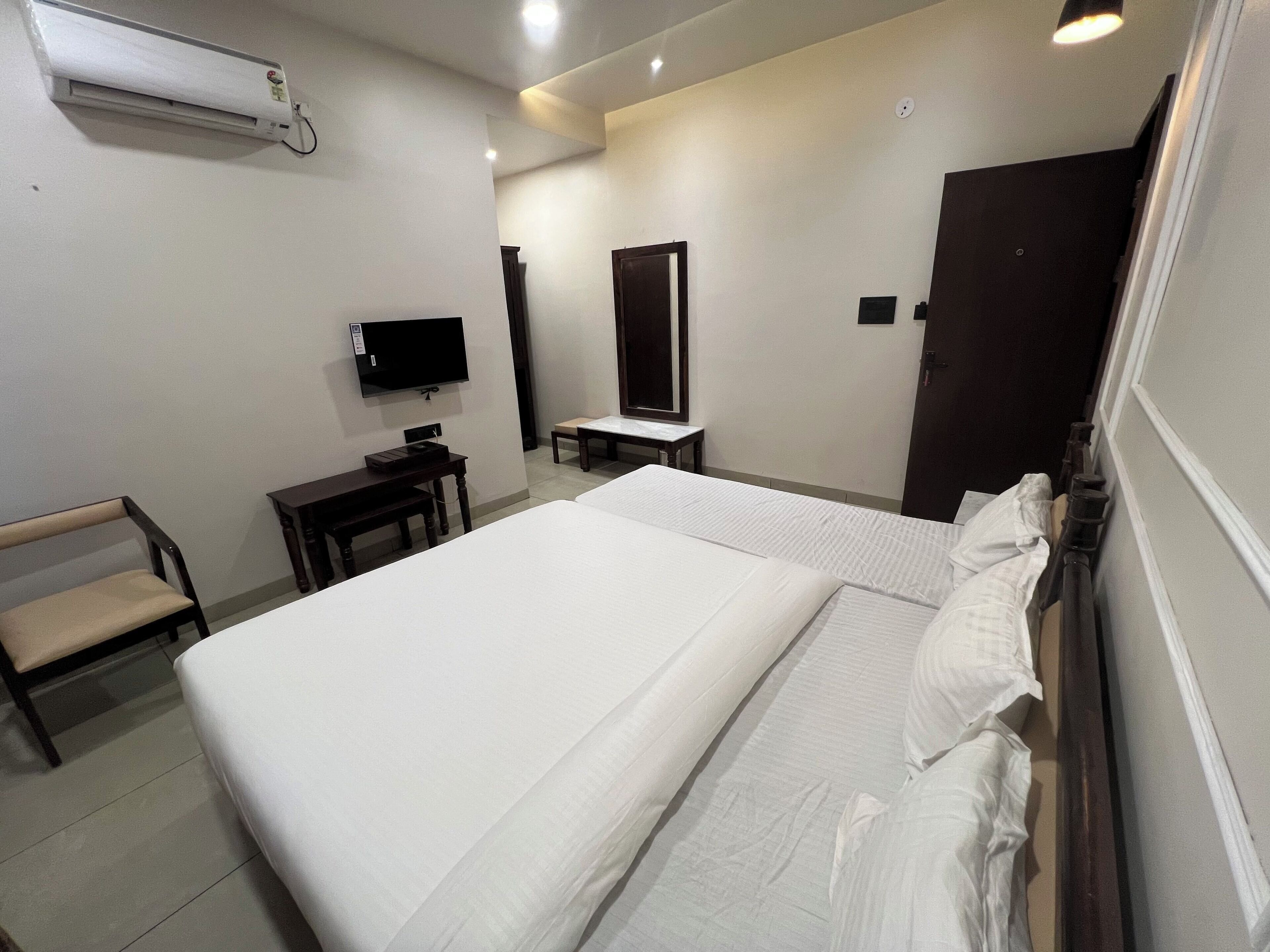 Una habitación de hotel con cama, escritorio, silla, televisión y espejo.