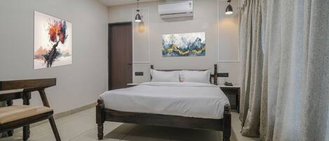 Un dormitorio con cama, dos mesitas de noche, un banco, un aire acondicionado y dos lámparas de pared.
