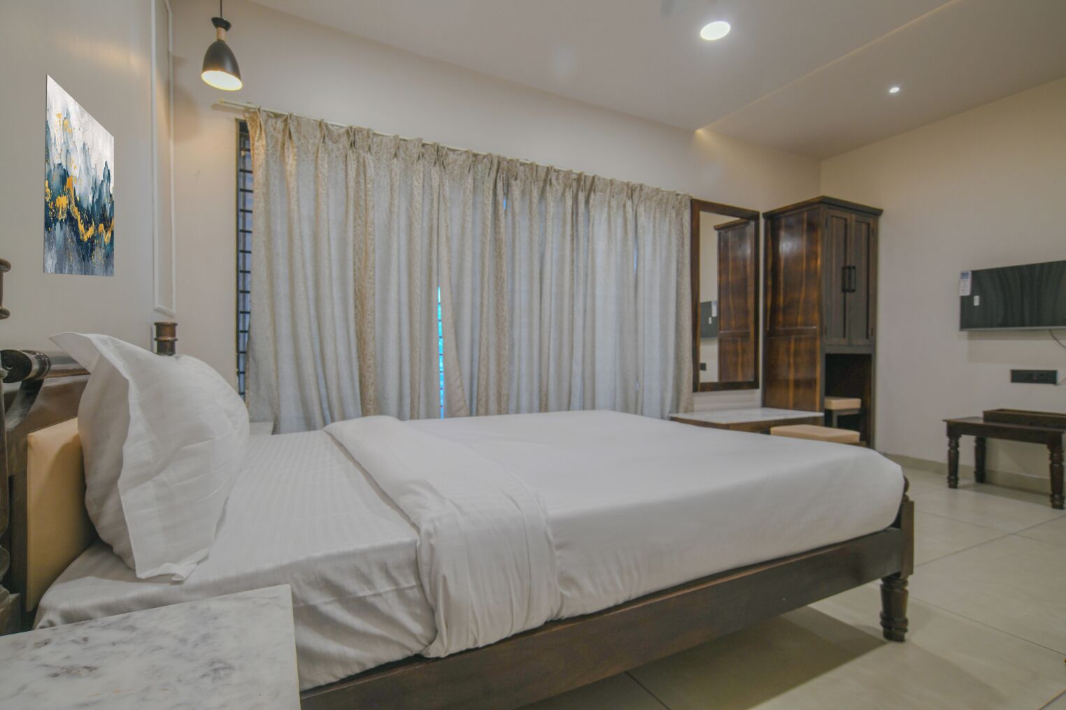 A bedroom with a large bed, a bedside table, a wardrobe, and a television on the wall.
