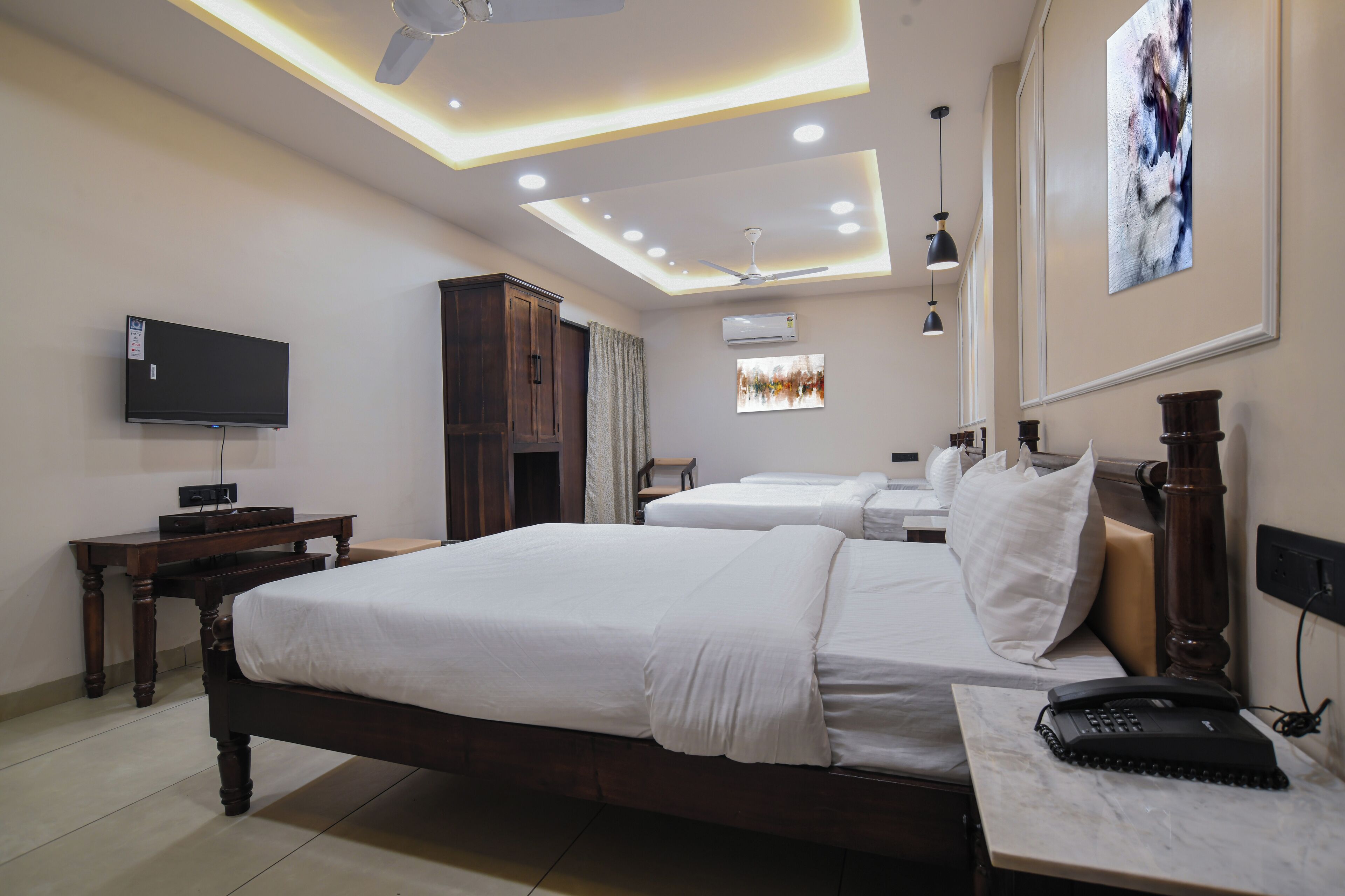 A hotel room with a large bed, a desk, a flat-screen TV, a ceiling fan, recessed lighting, and a painting on the wall.