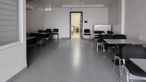 Ein geräumiger Konferenzraum mit Tischen, Stühlen, einem Deckenventilator, eingelassener Beleuchtung und einer Tür zu einem weiteren Bereich.