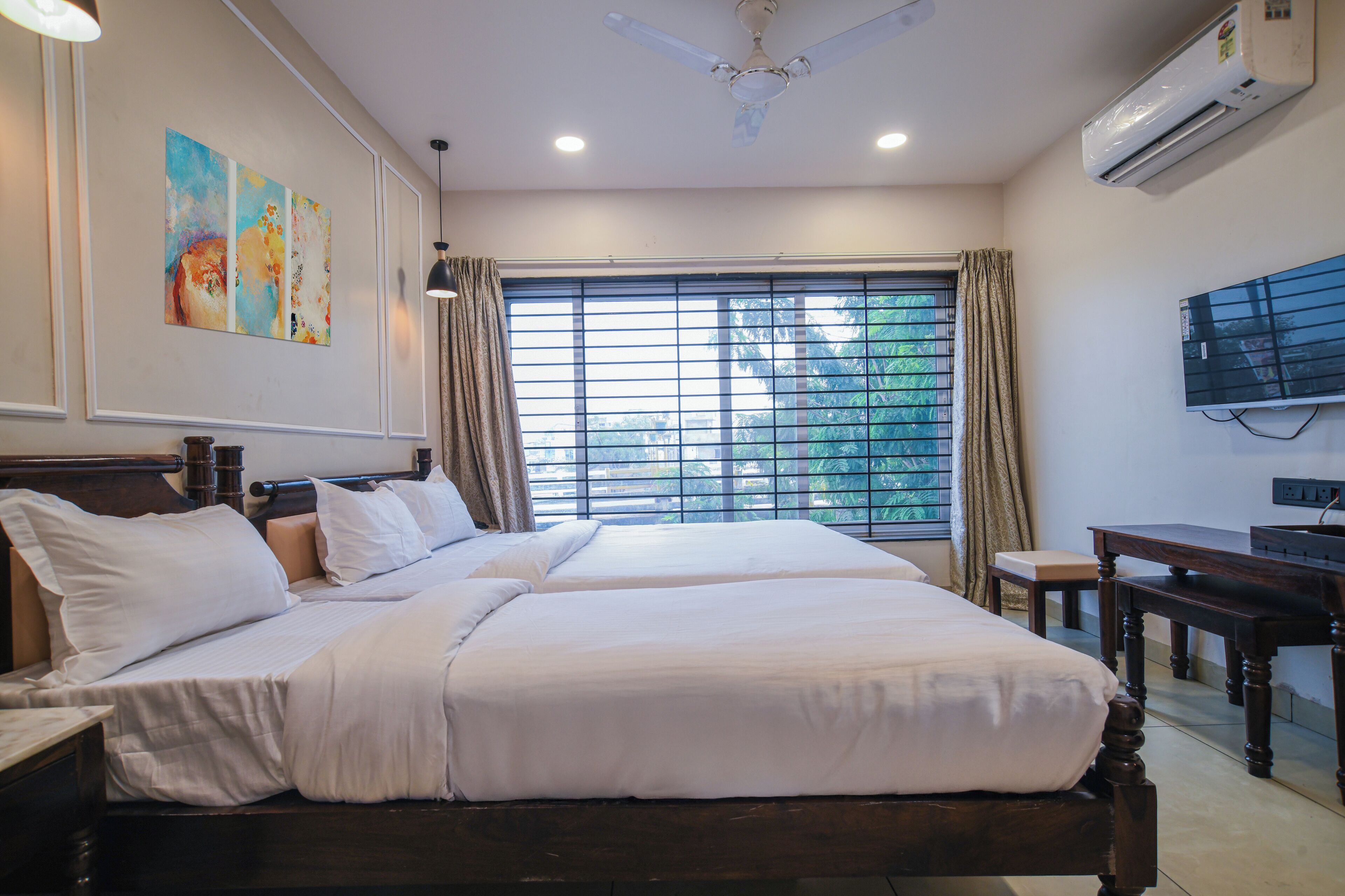 A hotel room with two beds, a desk, a TV, and a window with curtains.