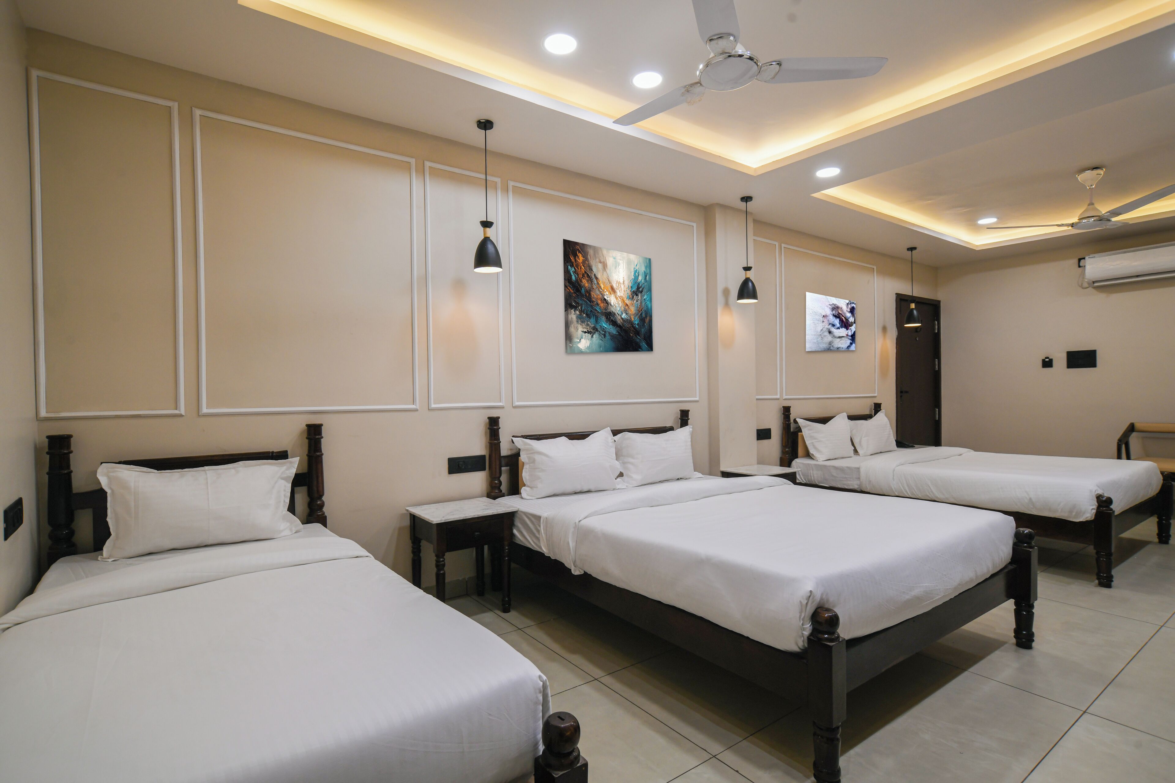 A hotel room with three single beds, a ceiling fan, recessed lighting, and artwork on the walls.
