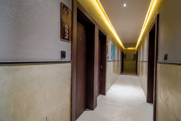 A hotel hallway with wooden doors, a clock, and a sign indicating room number 002.