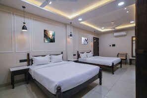 Une chambre d’hôtel avec deux lits, un ventilateur de plafond, un éclairage encastré et des œuvres d’art accrochées aux murs.