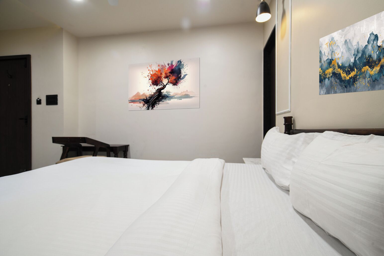 A hotel room with a large bed, a desk, and two artworks on the walls.