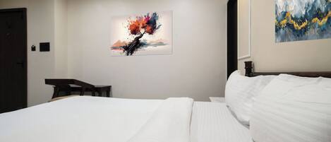A hotel room with a large bed, a desk, and two artworks on the walls.