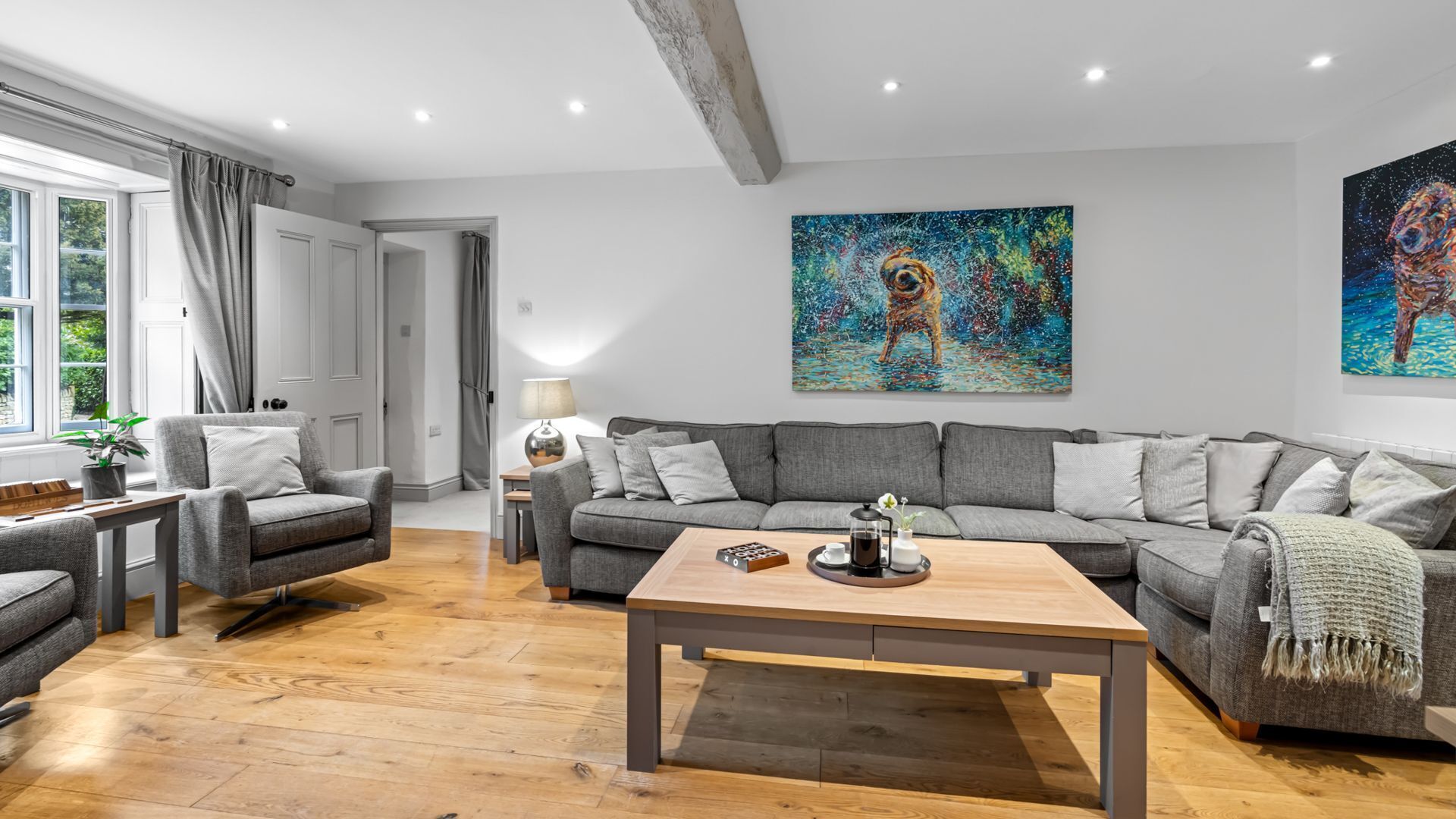 A modern living room with a grey sofa, a wooden coffee table, and a painting on the wall.