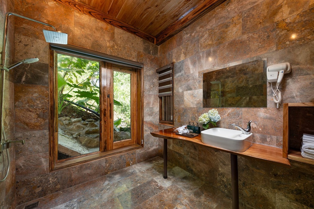 Un baño con pared de piedra, tocador de madera, ventana grande y ducha.