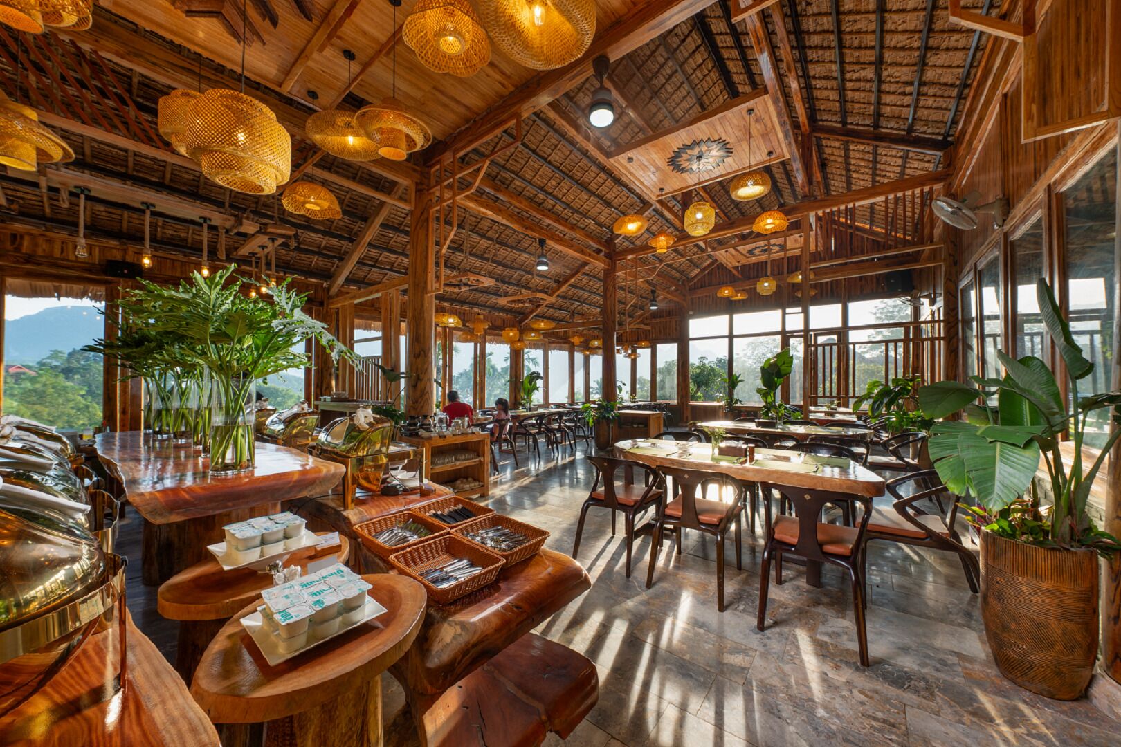 A spacious restaurant with wooden interiors, large windows, and hanging wicker light fixtures.