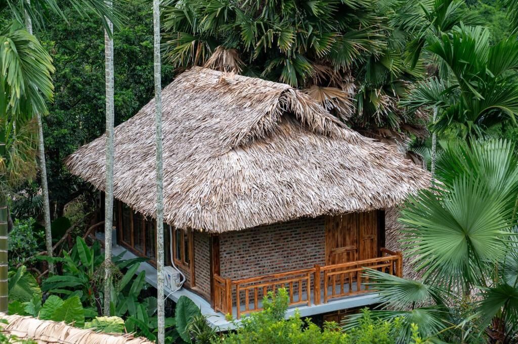 A thatched-roof hut with a wooden balcony, surrounded by lush tropical vegetation.