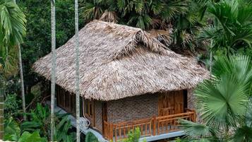 A thatched-roof hut with a wooden balcony, surrounded by lush tropical vegetation.