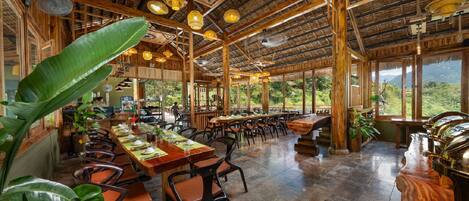 Un restaurante espacioso con techos altos, vigas de madera y grandes ventanales que ofrecen vistas al exterior.