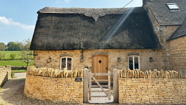 Un bâtiment en pierre avec un toit de chaume, une porte en bois et une enseigne sur laquelle on peut lire : « THE STUDIO ».