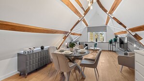 Un loft moderne avec des poutres en bois apparentes, un coin repas doté d’une table en verre et un espace salon confortable.