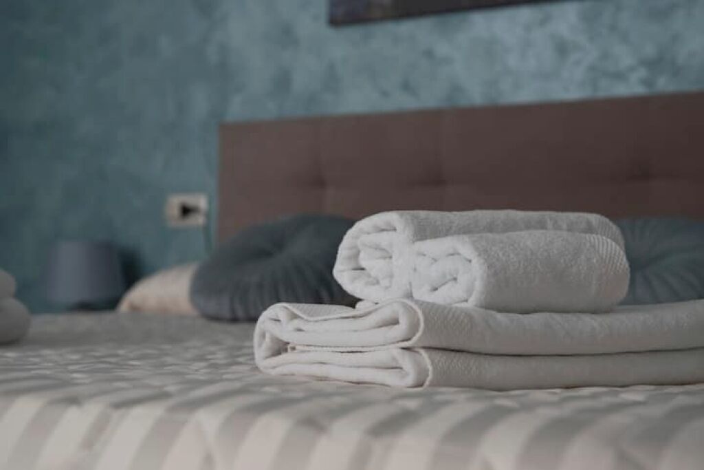 Un lit bien fait, avec des serviettes blanches pliées et un oreiller gris.