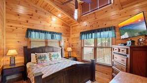 Een knus slaapkamer in een blokhut met een bed, een dressoir en een televisie aan een houten wand.