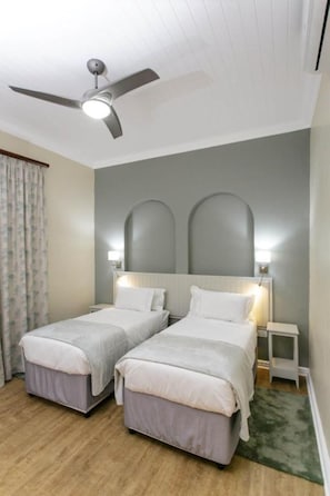 Quarto com duas camas de solteiro, um ventilador de teto e uma mesa de cabeceira com abajur.