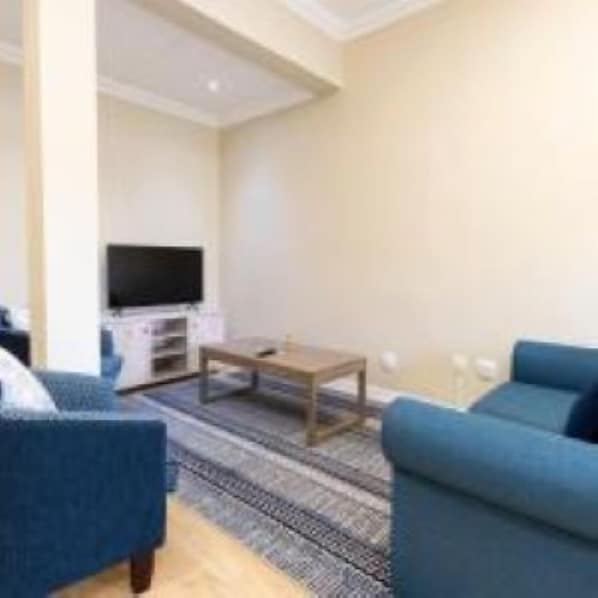 A modern living room with a sofa, a coffee table, and a flat-screen TV. - Queen's Residences by BON Hotels (Oudtshoorn)