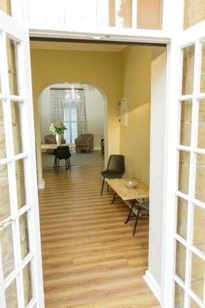 An open doorway leading to a room with a wooden floor, a dining table with chairs, and a window with curtains. - Queen's Residences by BON Hotels (Oudtshoorn)