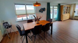 A dining area with a wooden table, black chairs, a hanging light fixture, and a view of the outdoors through large windows.