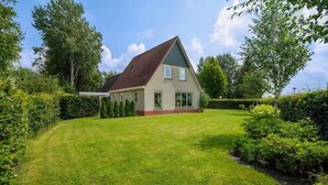 A single-story house with a sloped roof, surrounded by a well-maintained lawn and hedges.