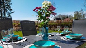 A dining table set outdoors with chairs, a vase of flowers, and blue plates and bowls.
