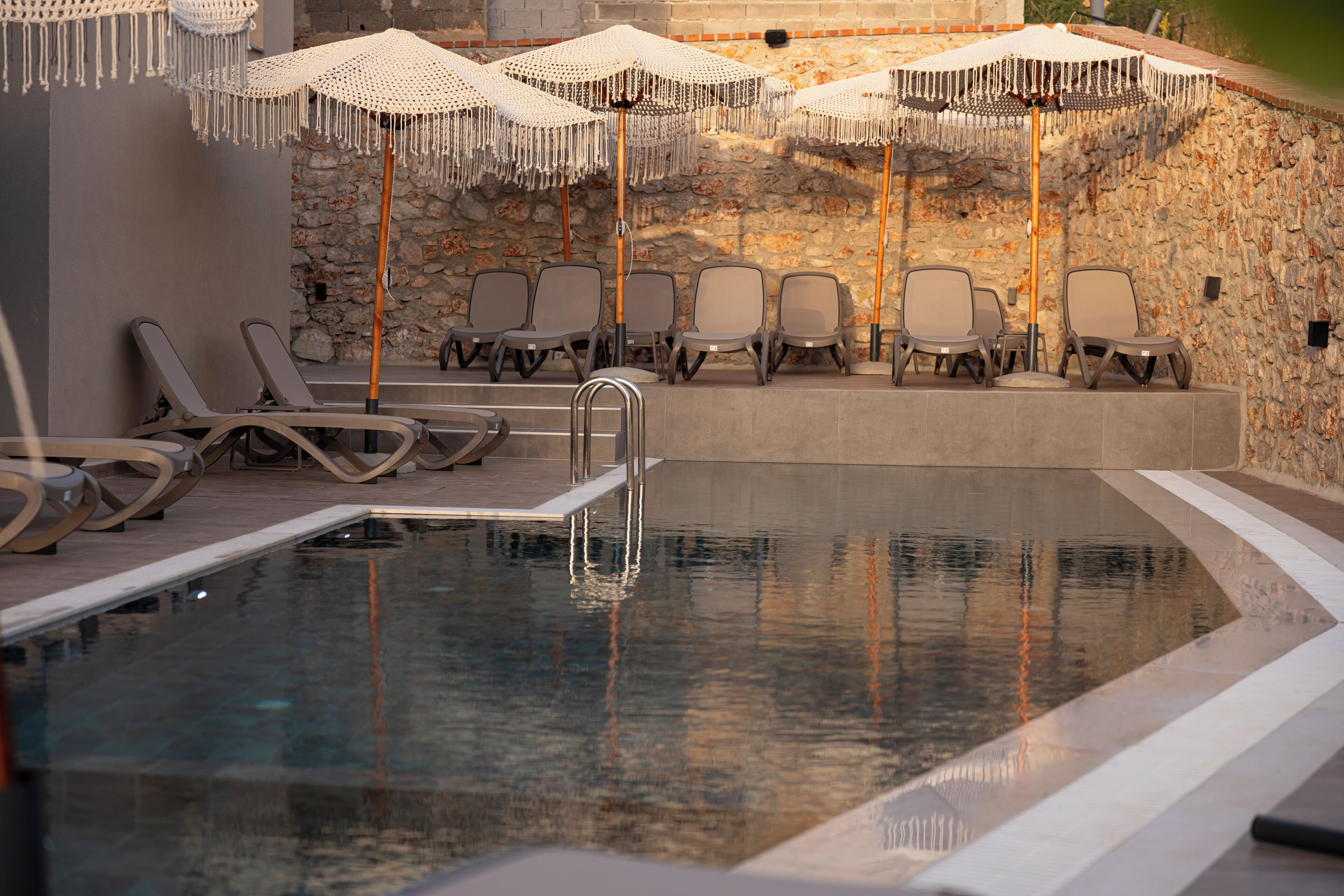 Un espace piscine avec des chaises longues et des parasols, un mur en pierre et une eau cristalline.