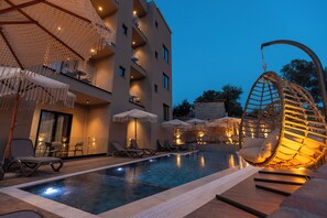 A pool area with lounge chairs and umbrellas, a hanging chair, and a building with balconies. - Diol Hotel (Ksamil)