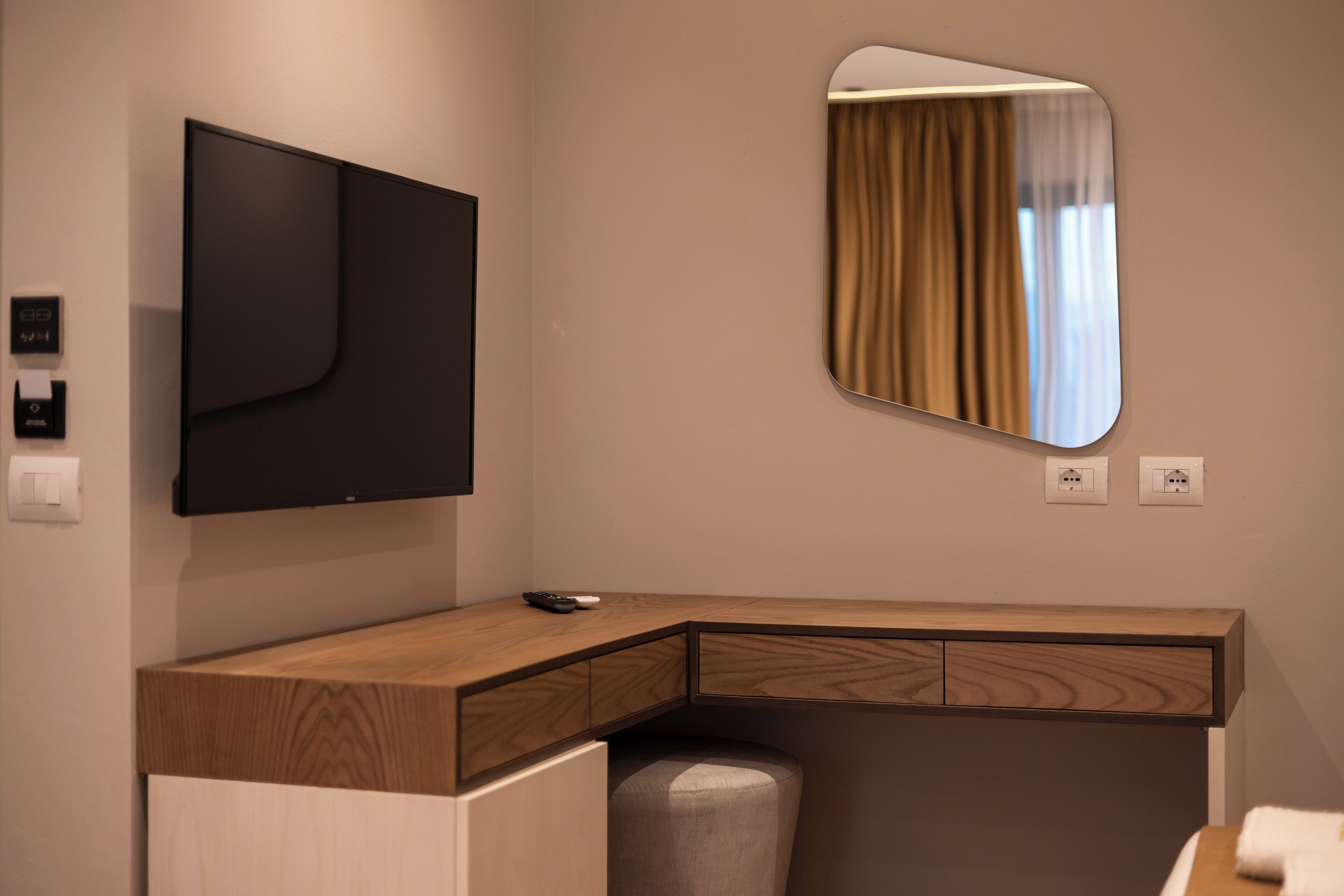 A modern room with a wooden desk, a flat-screen TV, a mirror, and a small seating area.