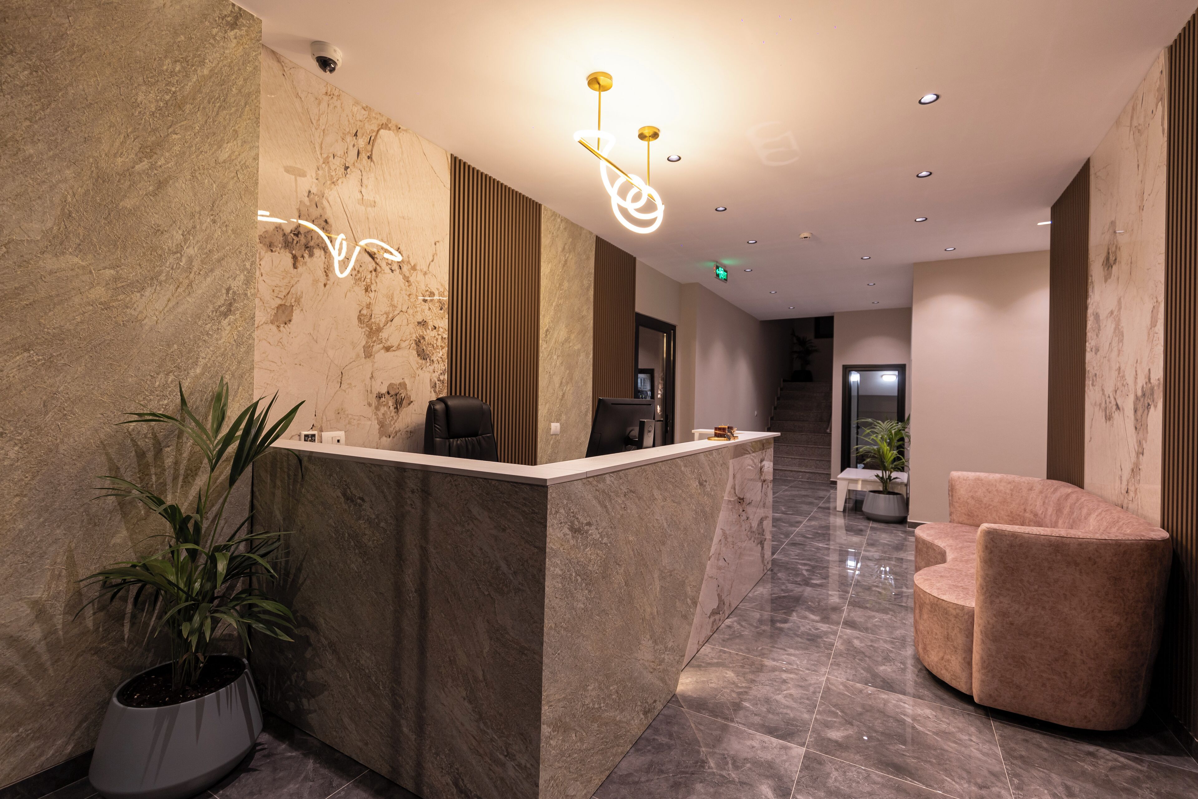 A reception area with a marble reception desk, a potted plant, a modern chair, and a staircase in the background.