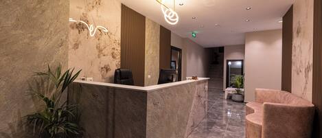 A reception area with a marble reception desk, a potted plant, a modern chair, and a staircase in the background.