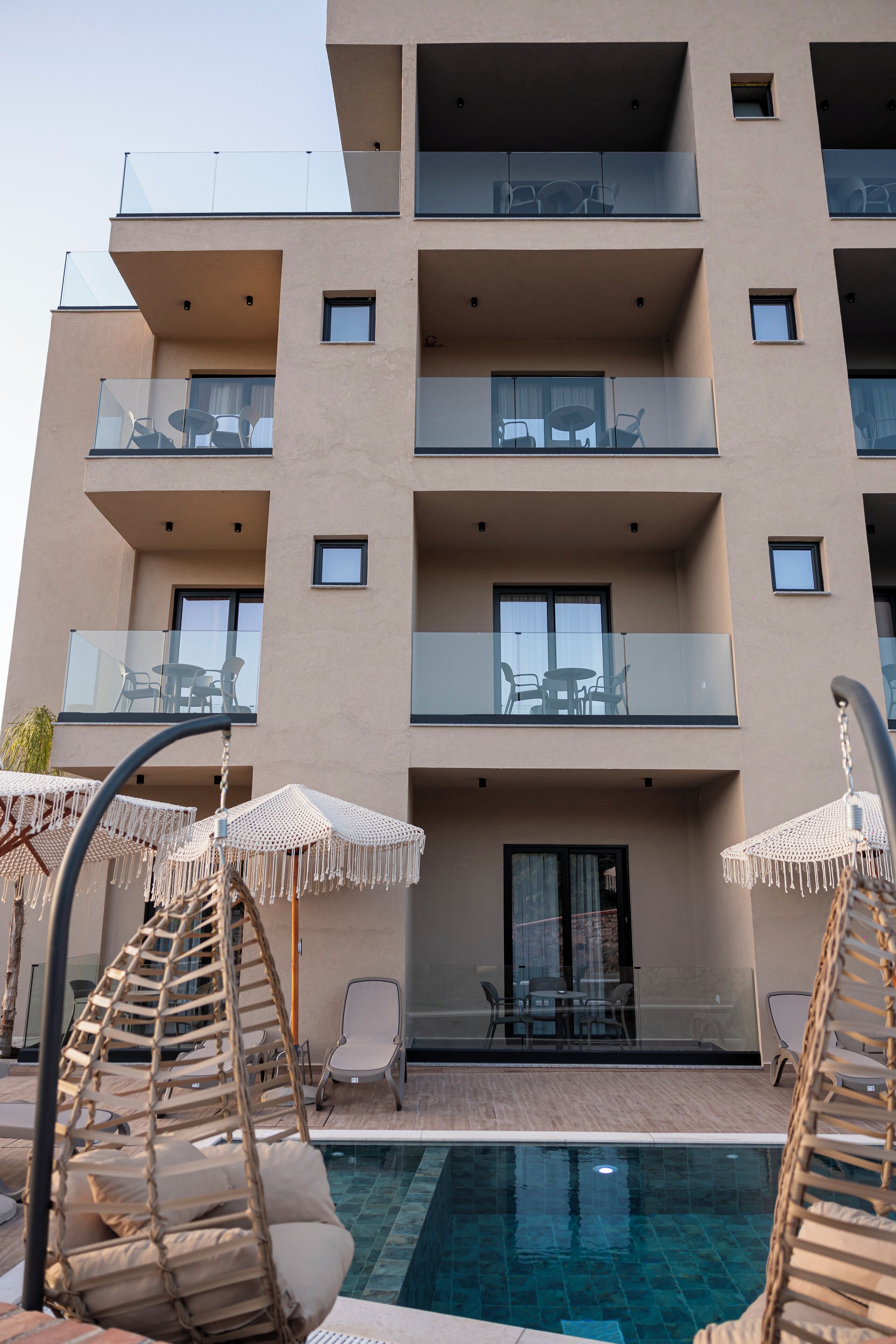 A modern building with multiple balconies, outdoor seating, and a swimming pool.