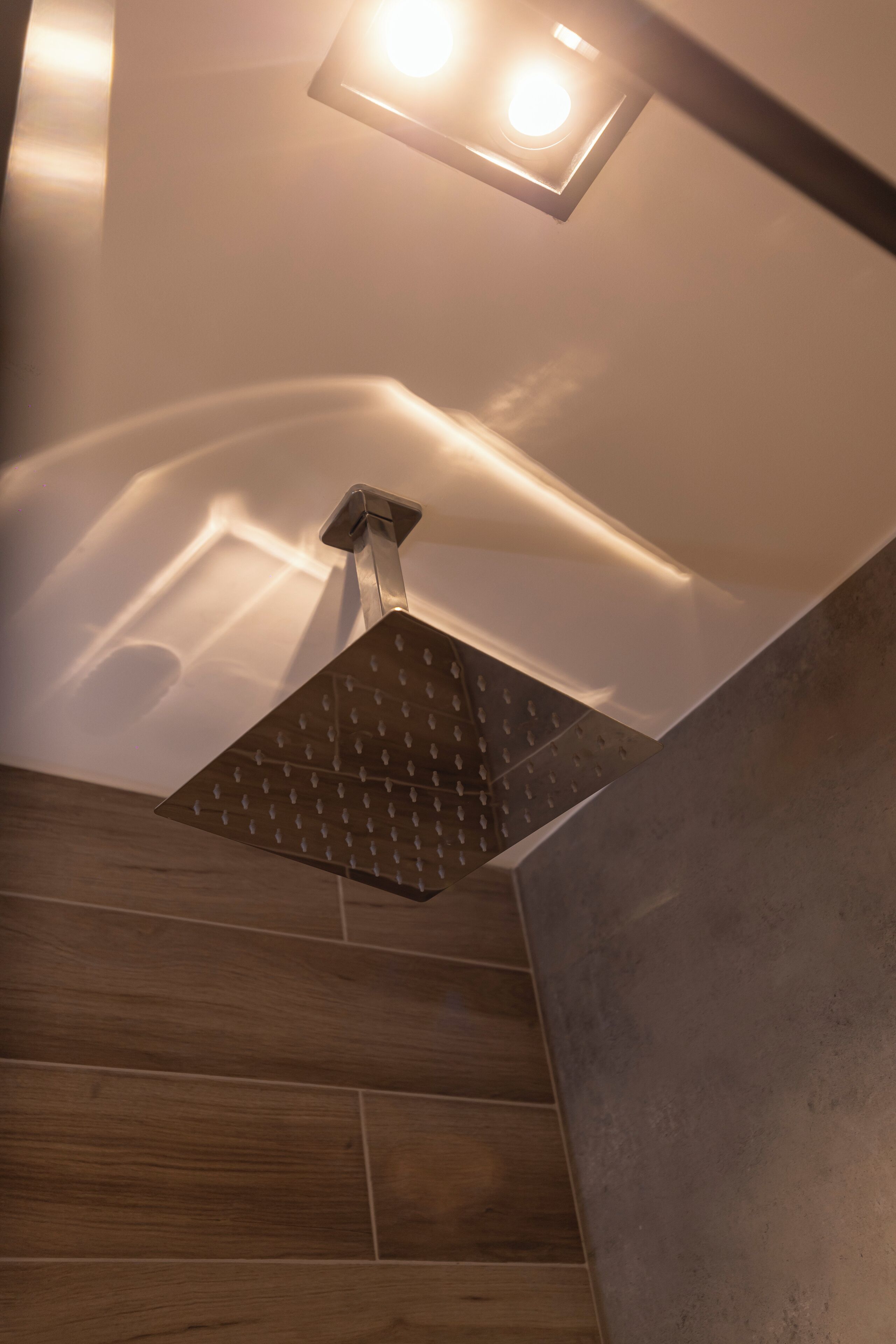 A modern shower with a square design and a ceiling light fixture above it.