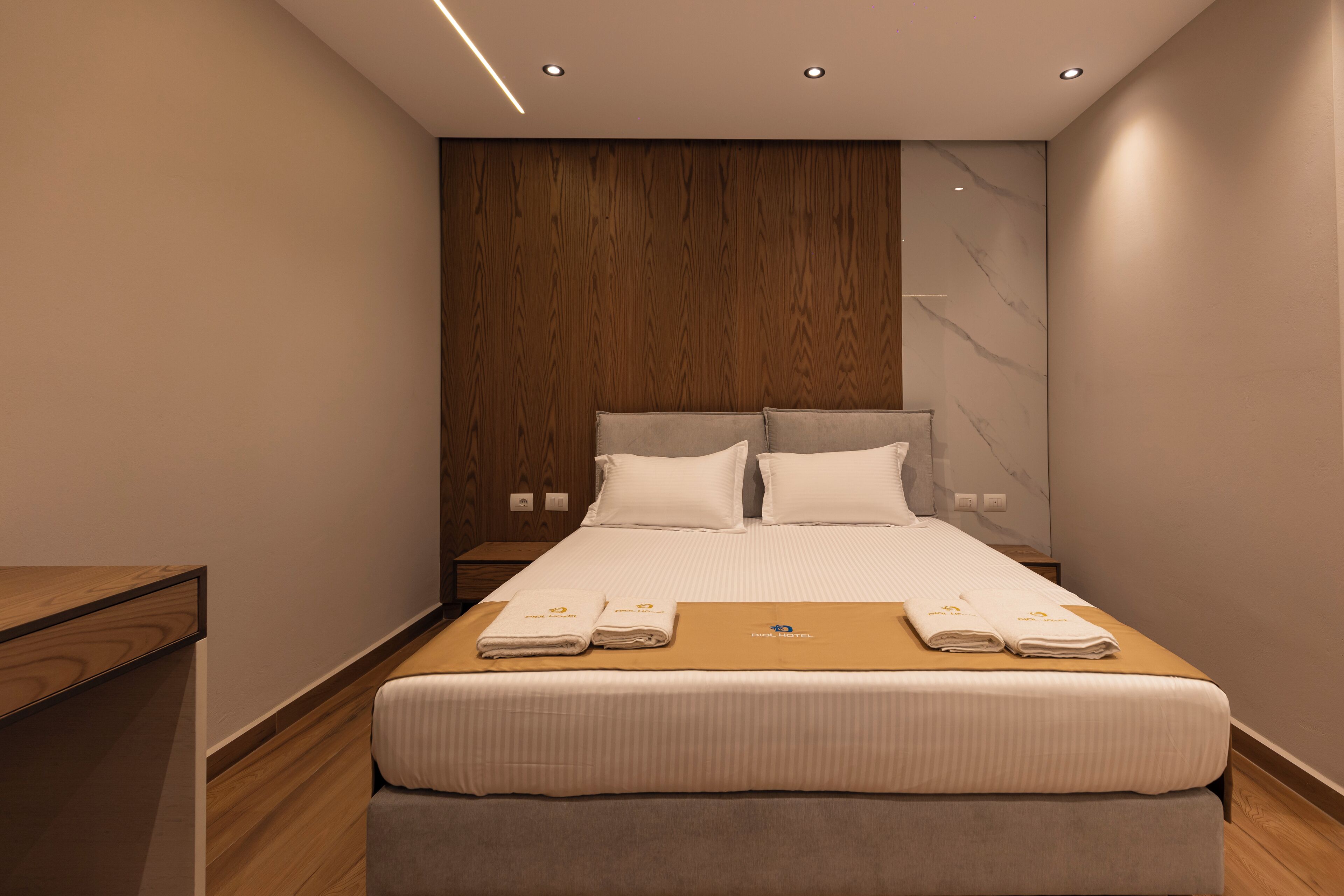 Une chambre d’hôtel moderne avec une tête de lit en bois, un grand lit avec du linge de lit blanc et un banc en bois au pied du lit.